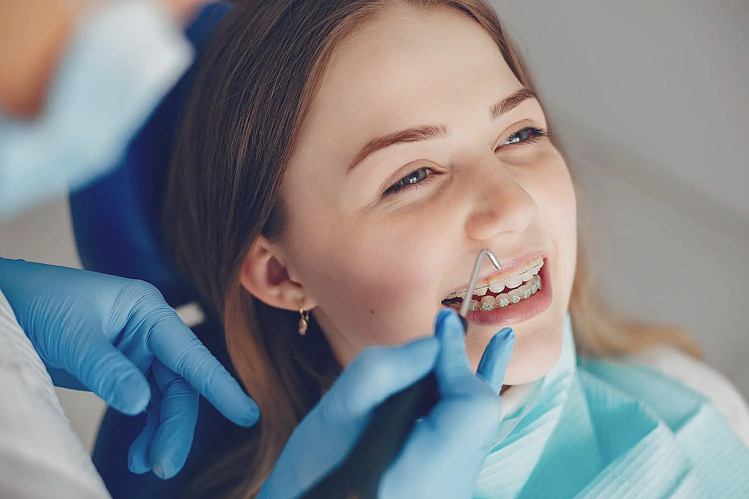 A person with braces gets dental care from a professional wearing blue gloves, while sitting in a dental chair in Sammamish, WA.
