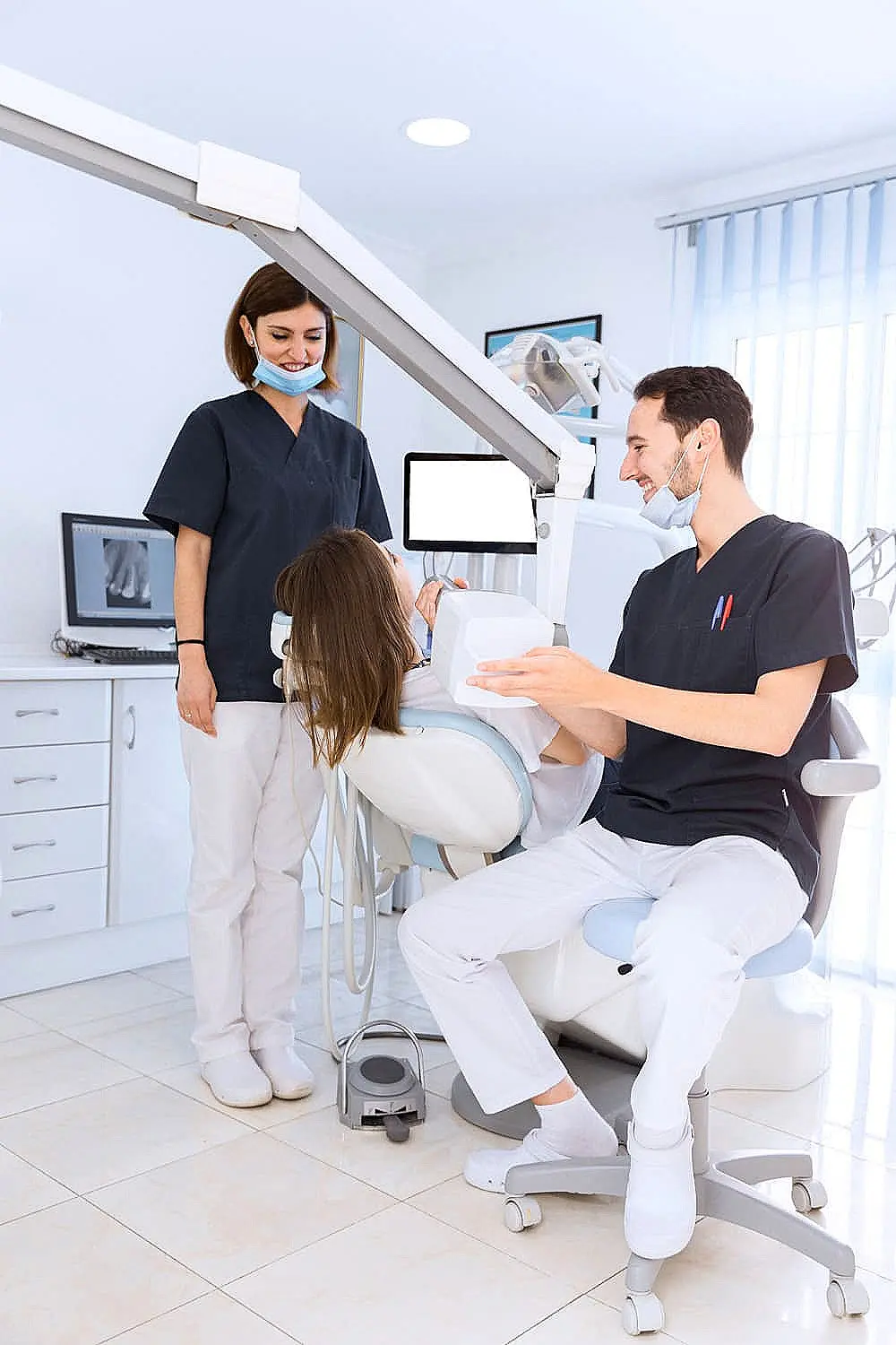 Dentist and assistant examine a patient in a dental clinic, using medical equipment. All are wearing masks and scrubs in Sammamish, WA..
