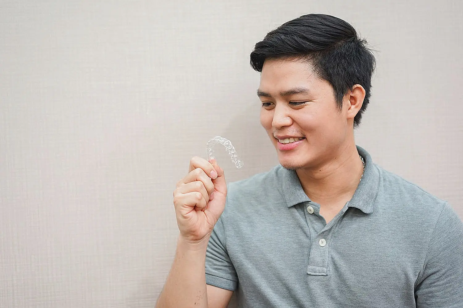 Person in a gray polo shirt holding a clear dental aligner in Sammamish, WA.