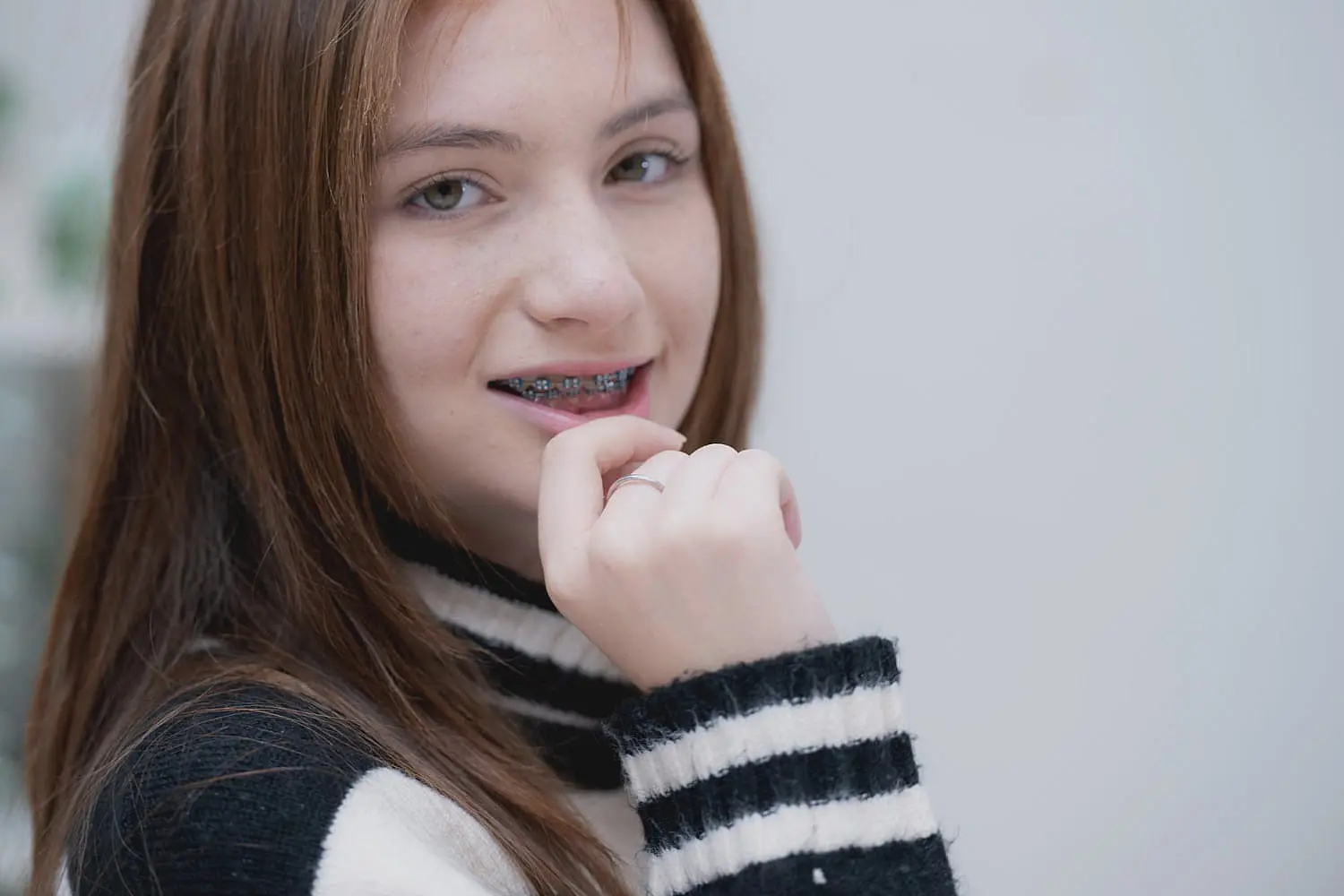 A person with braces, wearing a striped sweater, is looking at the camera with a slight smile and resting their hand on their chin in Sammamish or Kent, WA.
