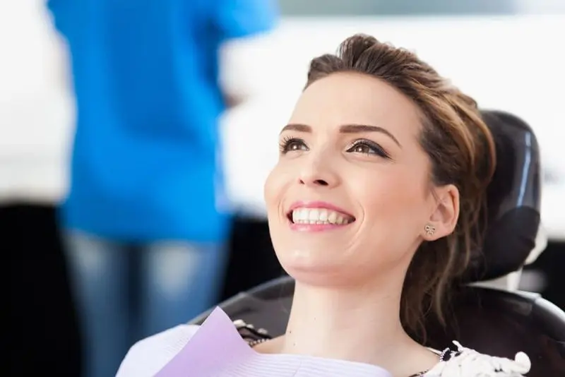 A person with brown hair and a purple dental bib smiling while sitting in a dental chair for her lingual braces (InSmile, formerly InBrace) in Sammamish or Kent, WA