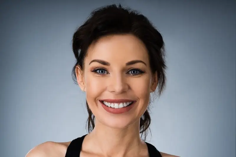 A person with dark hair, proudly showcasing their clear braces, smiles broadly while facing forward against a plain background in Sammamish, WA.