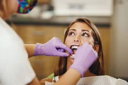 An orthodontist in Sammamish or Kent, WA, examines a woman's teeth with a dental mirror and probe. The patient is seated comfortably, while the dentist dons purple gloves.