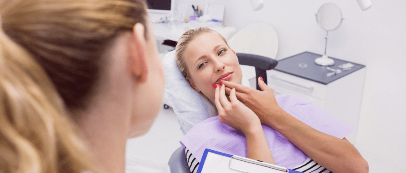 A woman with adult braces sits in a dental chair, touching her lips while talking to a dentist holding a clipboard in a dental office in Kent or Sammamish, WA.