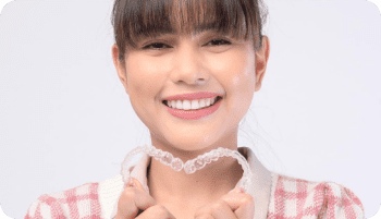 A person smiling and holding Invisalign clear aligners in both hands, positioned in front of their mouth in Kent or Sammamish, WA.