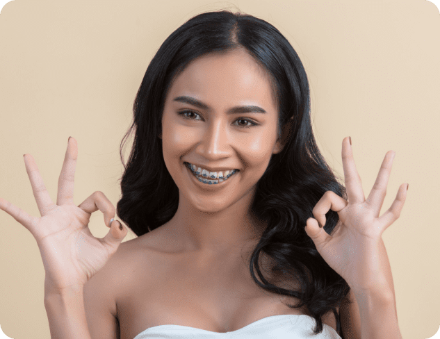 Woman with long dark hair and adult braces smiling at the camera while making an "OK" hand gesture with both hands in Kent or Sammamish, WA.