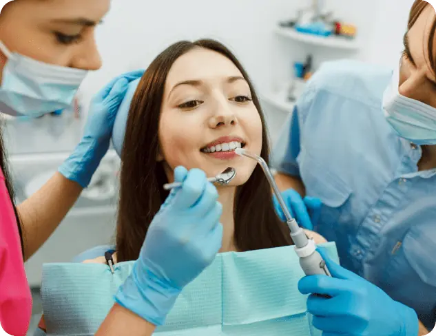 A woman sits in a dental chair while two dental professionals wearing gloves and masks work on her teeth with dental instruments, highlighting expert care for Adult Braces in Kent, WA.