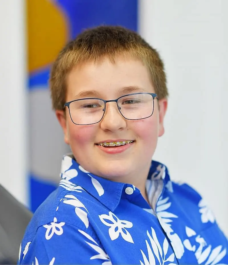 A smiling person with glasses and braces, wearing a blue floral shirt, showcases their bright smile courtesy of Freelove Orthodontics in Sammamish, WA.