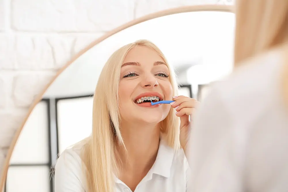 young woman metal braces toothbrush home - How to Floss with Braces in Kent and Sammamish, WA