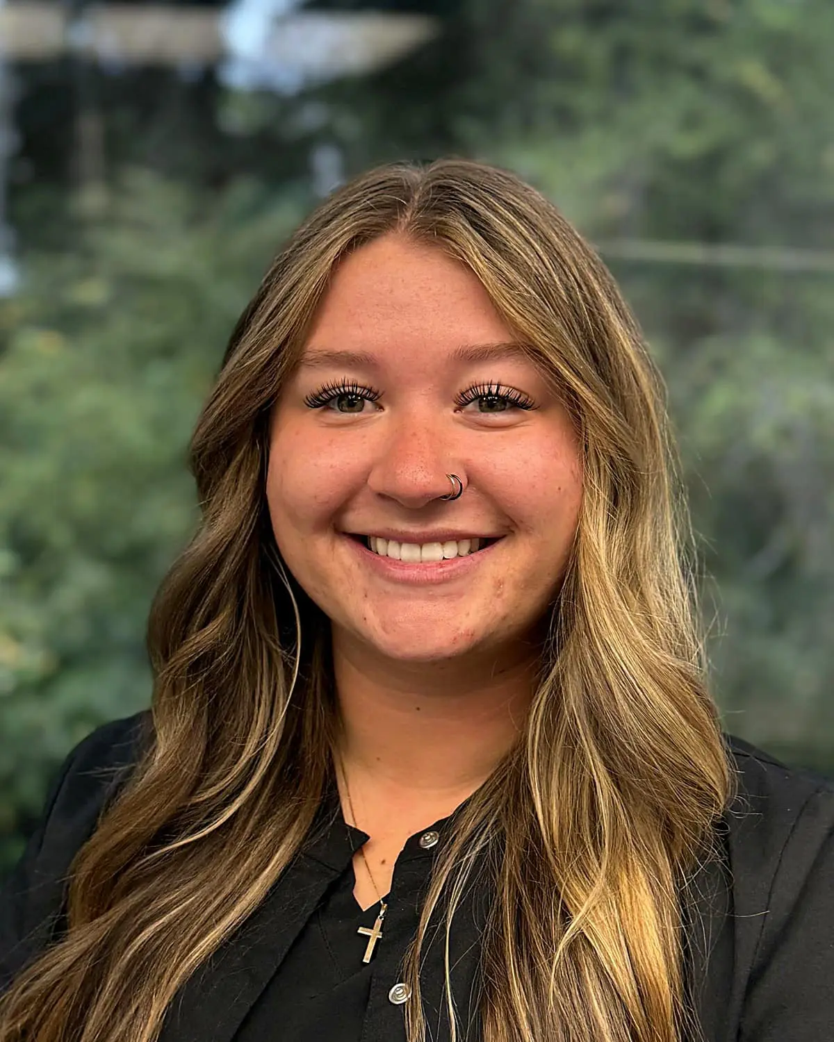 Bailey, a young woman with long light brown hair, a nose ring, and a black shirt, smiles outdoors in front of greenery at Freelove Orthodontics in Kent or Sammamish, WA.